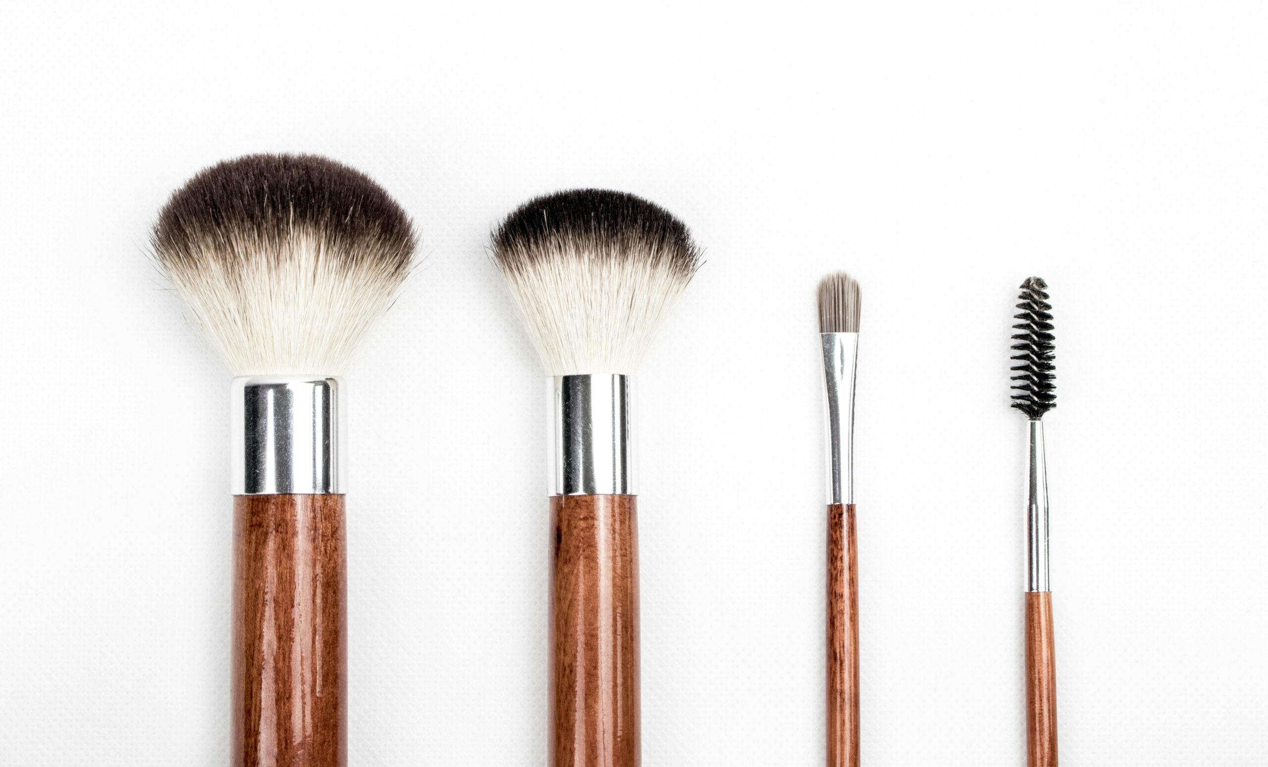 Stylish flat lay of four wooden makeup brushes against a clean white background.